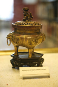 A coppery incense burner on a wooden base with carving of a dog on its top