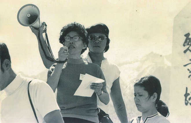 Three people gather around a woman speaking with a bull-horn.